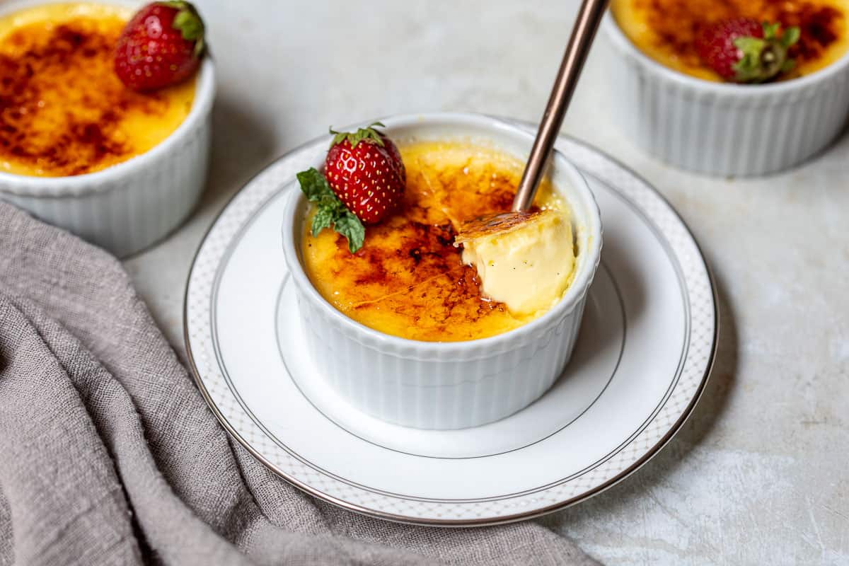 creme brulee in a ramekin on a small plate in front of two other ramekins.