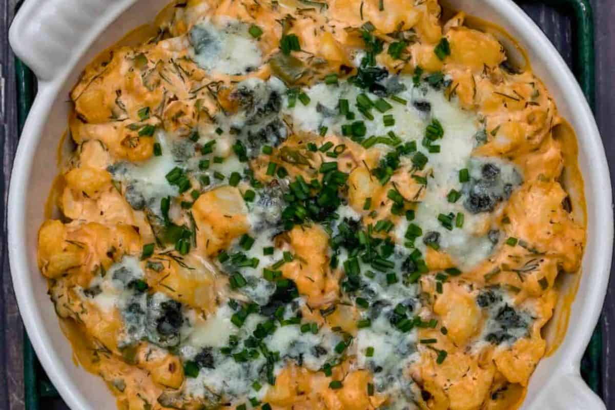 Baked gnocchi in a round dish topped with melted cheese, herbs, and fresh chopped chives—these crowd-pleasing snacks are sure to score big as irresistible game day bites.