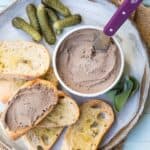 ramekin with chicken liver pâté next to crostini and cornichons and sage.