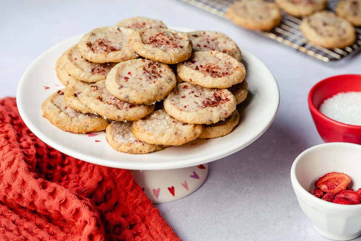 platter of strawberry shortbread cookies next to napkin and bowls of dried strawberries and sugar.