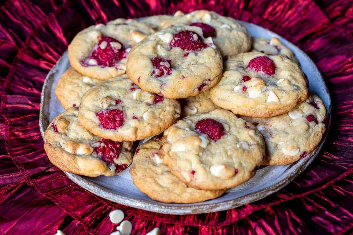 plate with pile of raspberry white chocolate cookies on red ruffled fabric.