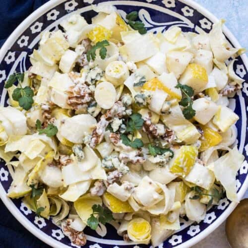 A salad with chopped endive, walnuts, blue cheese, pears, and fresh herbs served on a patterned plate.