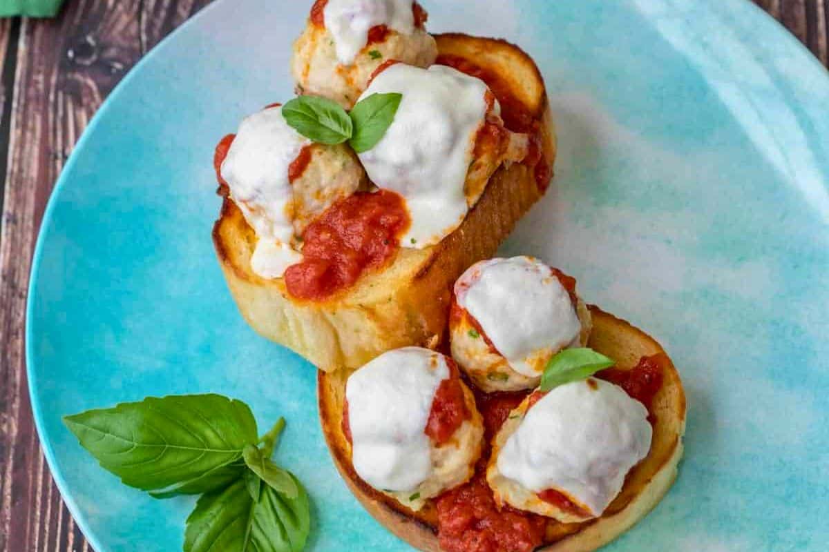 Two slices of toasted bread topped with chicken meatballs, tomato sauce, melted cheese, and basil leaves on a blue plate—perfect for easy recipes or quick weeknight meals.