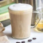 Vanilla Bean Latte next to three coffee beans and a small glass jar with vanilla simple syrup.