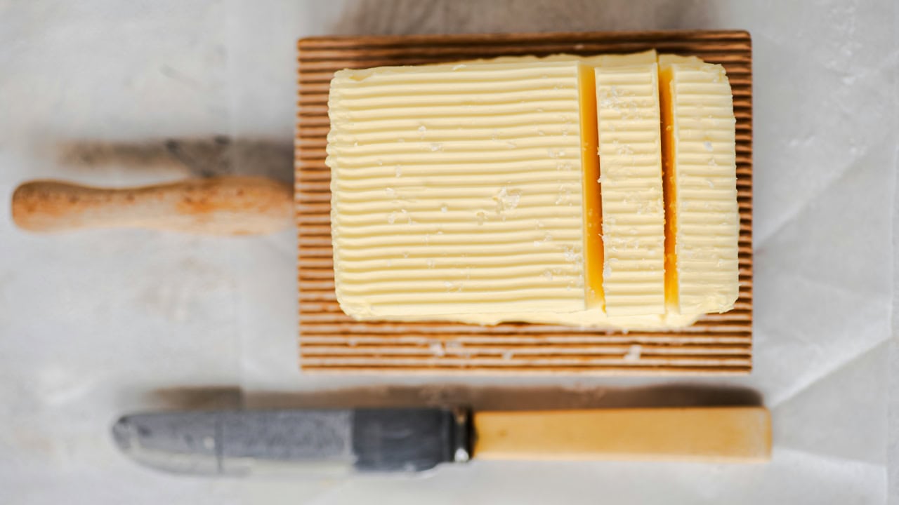 cube of butter in a butter wooden dish on a white paper horizontal perspective