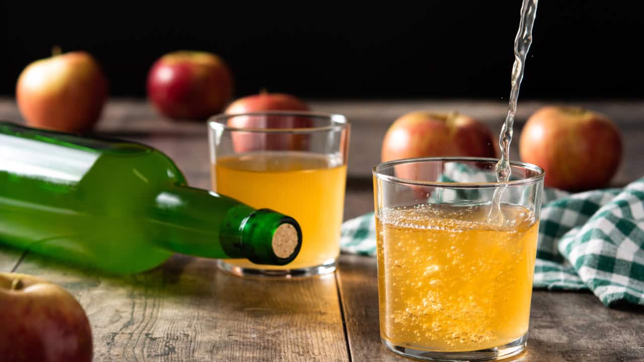 pouring-apple-cider-drink-into-glass-wooden-table