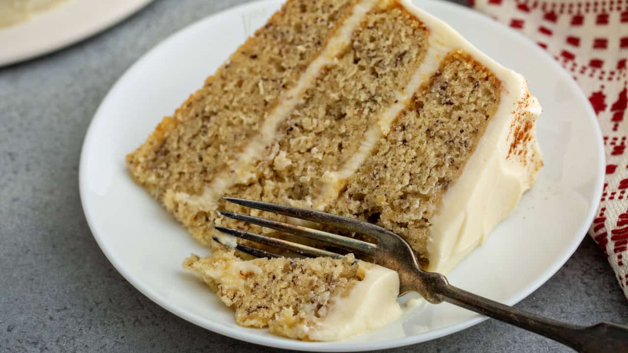 A person slices a homemade apple cake on a wooden board, showcasing its moist interior and crispy apple topping.