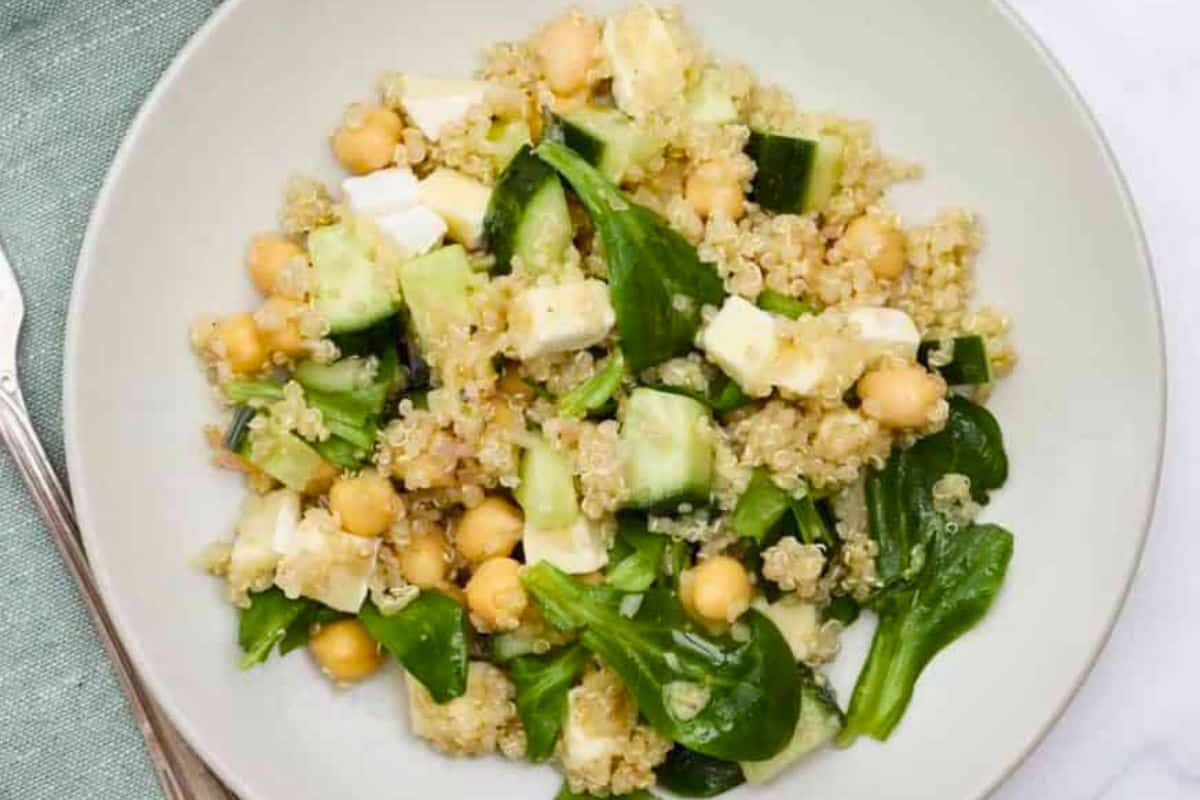 A plate of quinoa salad with chickpeas, spinach leaves, cucumber, and feta cheese on a white dish—a delicious addition to your collection of vegetarian recipes that’s meat eater friendly too.