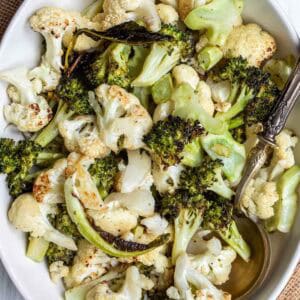 A bowl of roasted broccoli and cauliflower with a serving spoon.