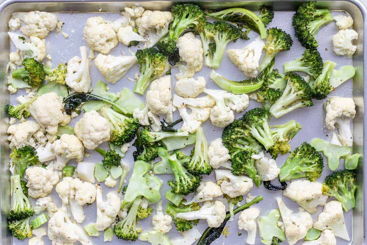 A baking sheet lined with parchment paper topped with partly-roasted cauliflower and broccoli florets.