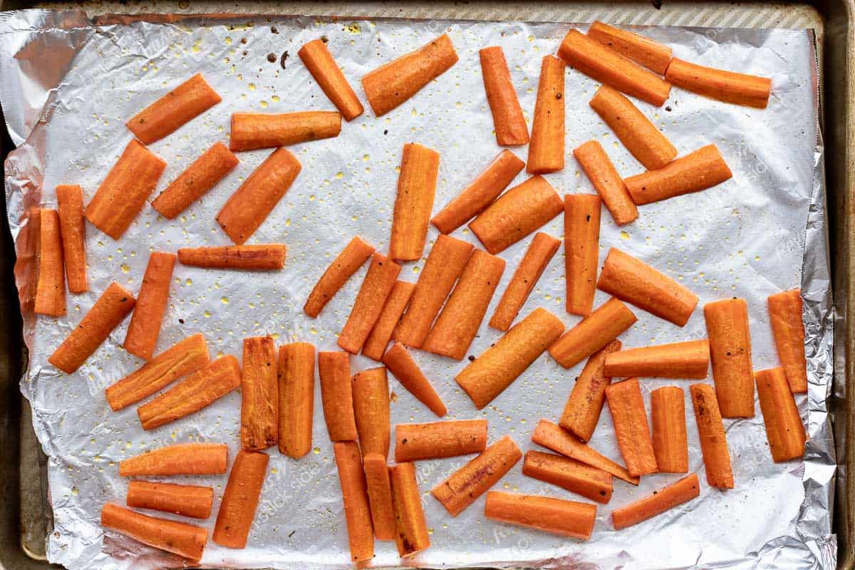 Chopped carrots roasted on a foil-lined baking sheet, seasoned with salt and pepper.