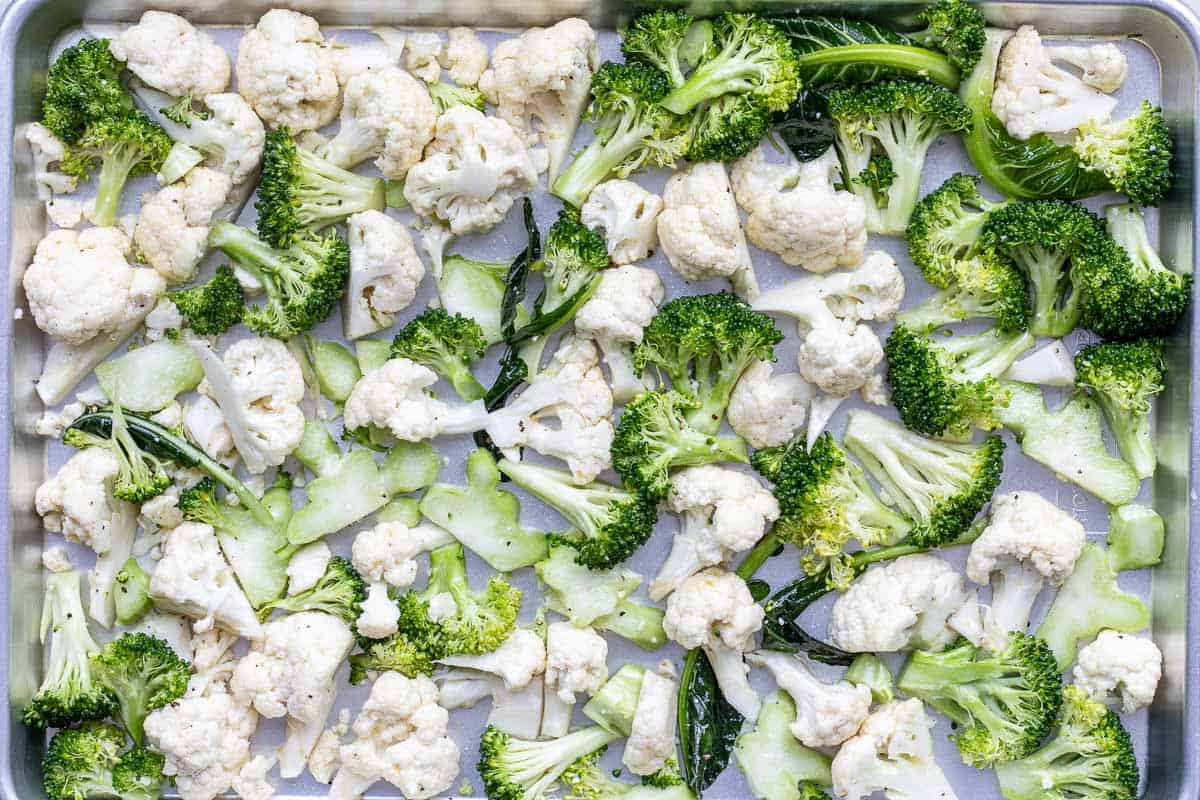 A baking sheet topped with raw cauliflower and broccoli florets spread out evenly, ready for roasting.