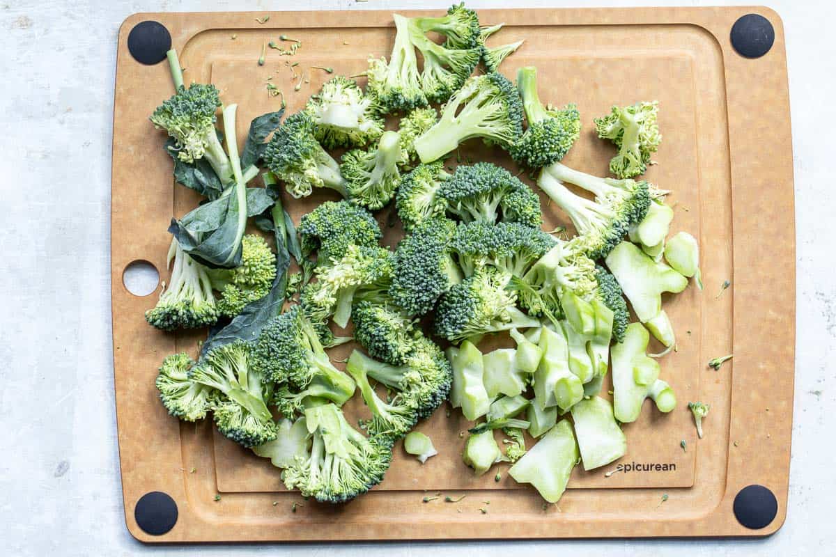 Chopped broccoli florets and stems on a brown cutting board with black corner grips.