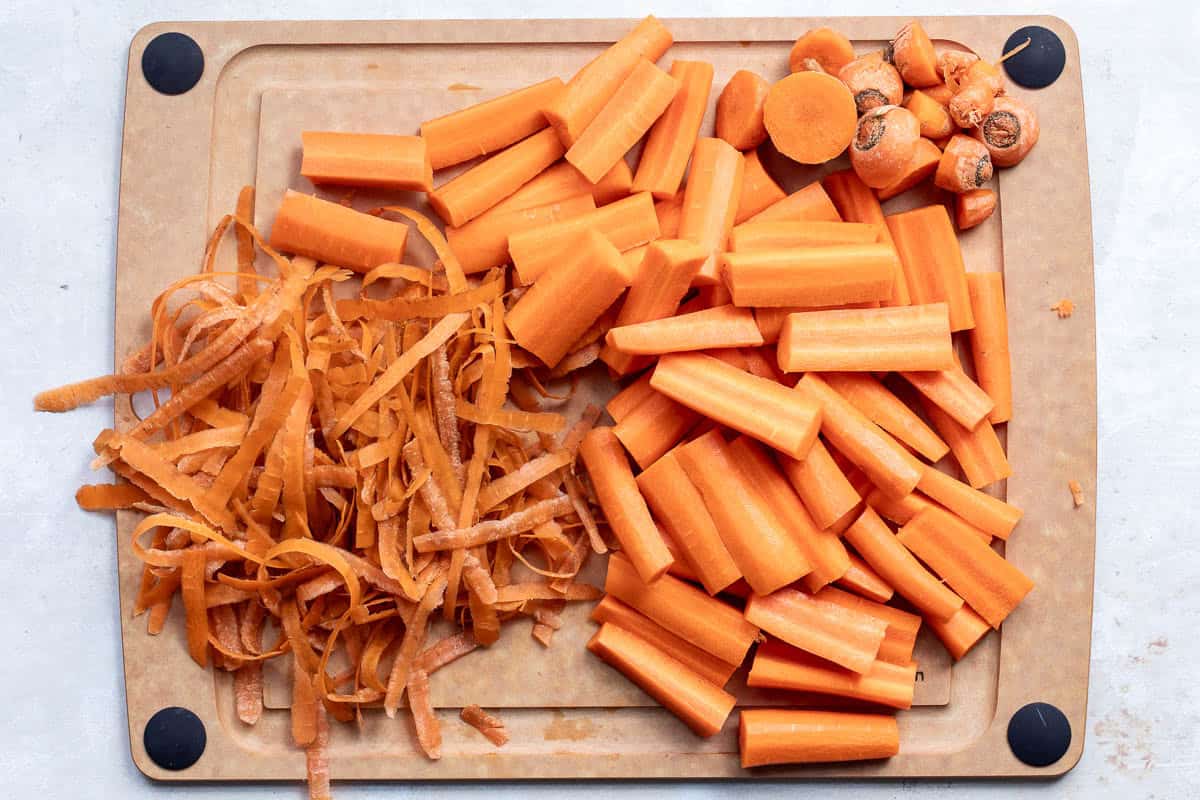 Chopped carrots, carrot tops, and carrot peels are arranged on a cutting board.