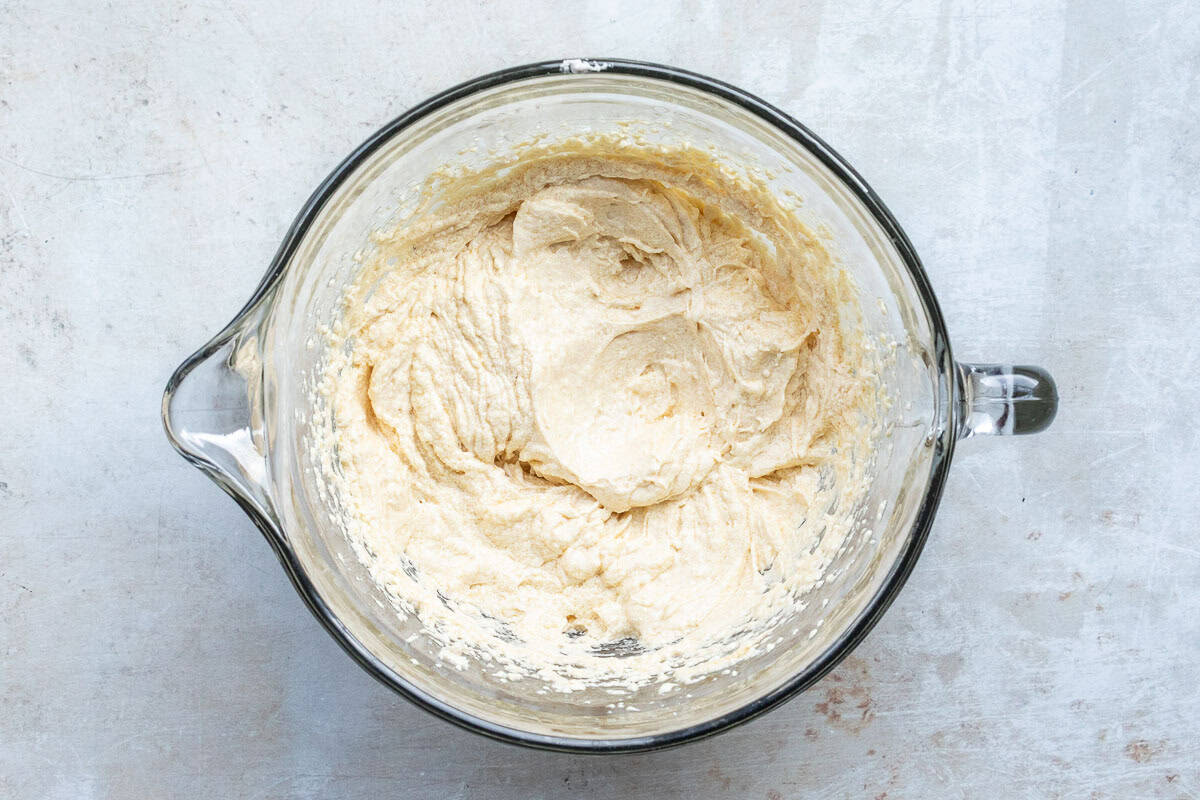 A glass mixing bowl filled with a pale, creamy batter, shown from above on a light gray surface.