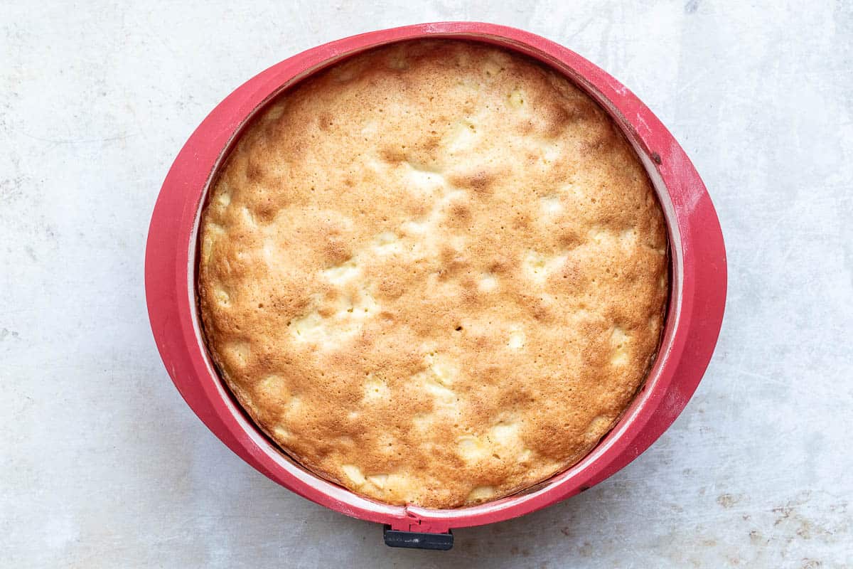 A French apple cake in a red silicone baking pan on a light-colored surface.