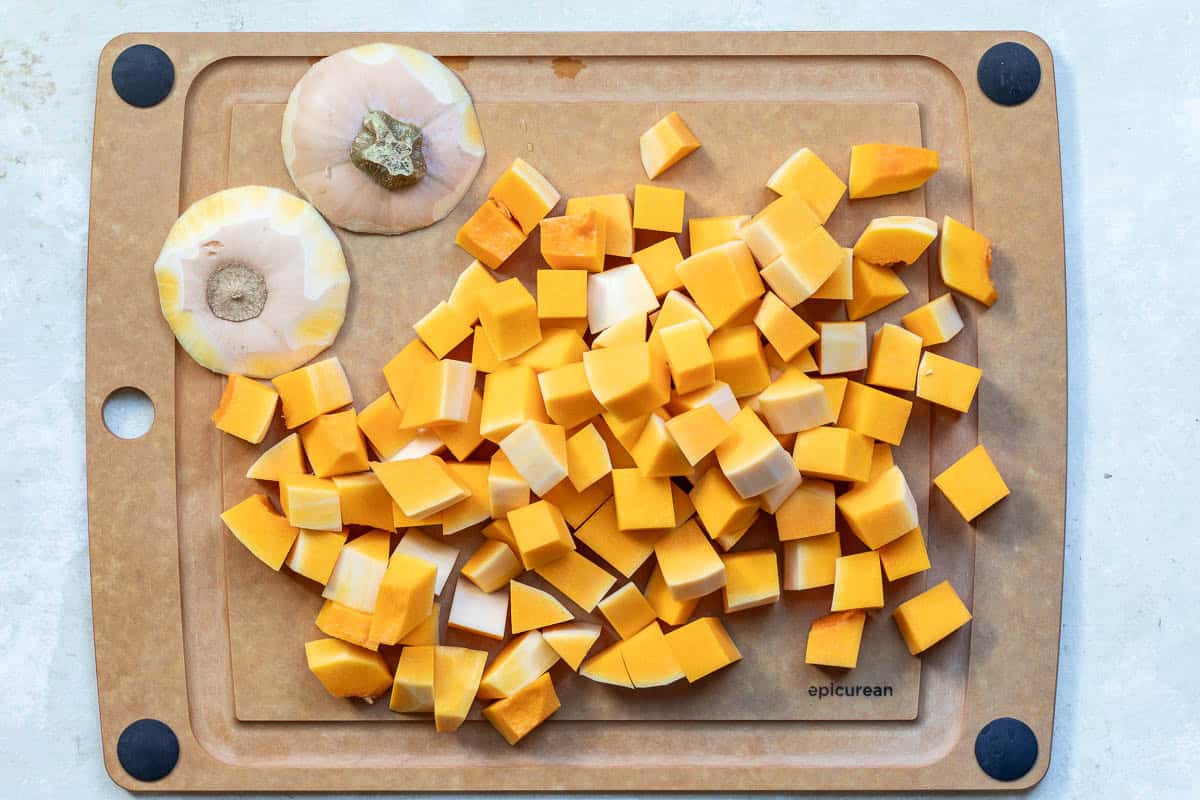 Diced butternut squash and two squash end pieces on a brown cutting board with black corner grips.