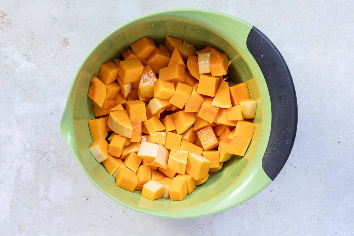 A green bowl filled with evenly cut cubes of raw butternut squash on a light-colored surface.