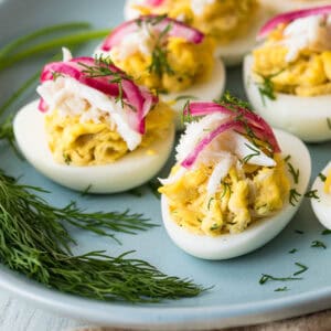 Deviled eggs topped with shredded crab, pickled red onions, and fresh dill are arranged on a plate with sprigs of dill on the side.