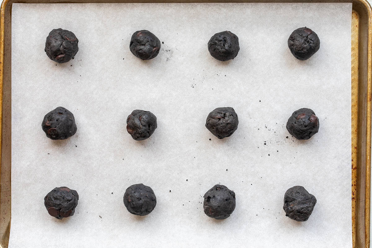 black cocoa cookie dough balls on a parchment lined baking sheet.