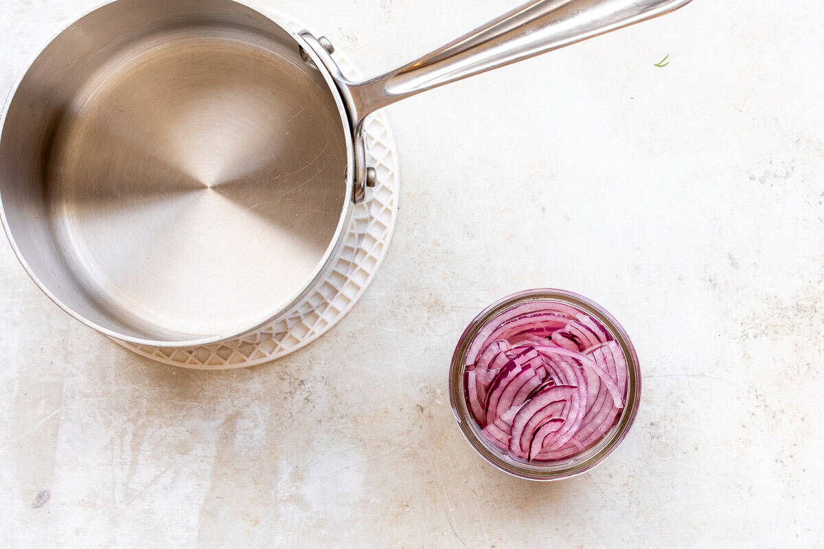 Pickling liquid in saucepan next to small mason jar with sliced red onions.