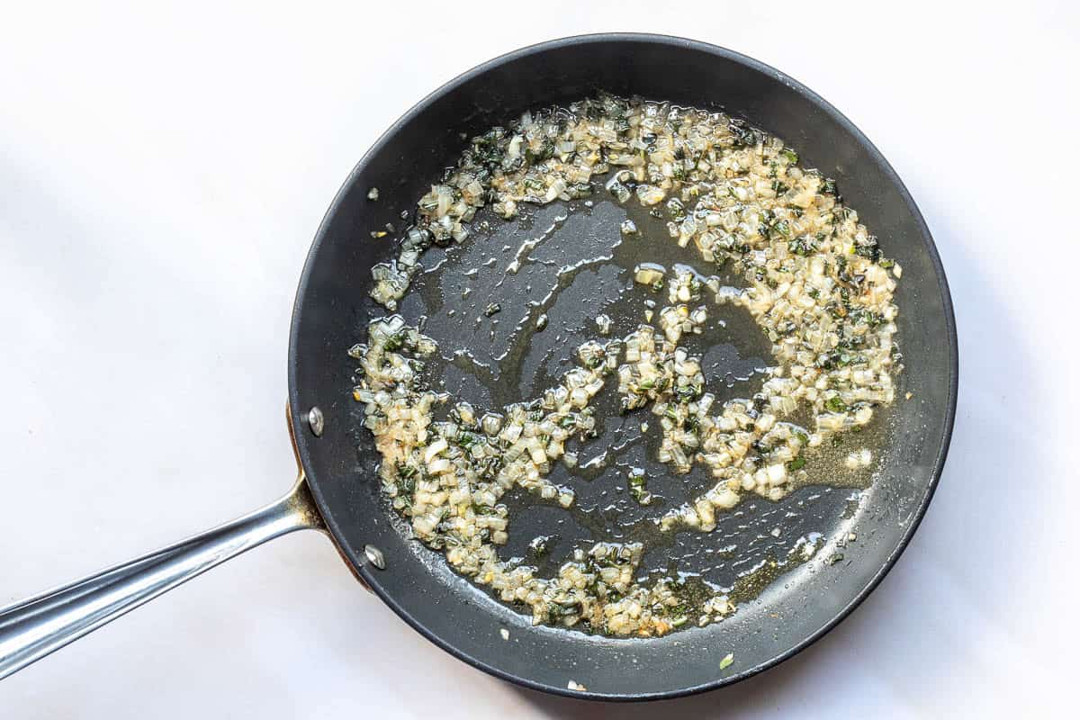A frying pan containing chopped shallots and sage being sautéed in oil.