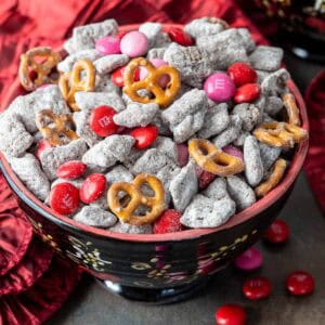 A bowl filled with Valentine's Day puppy chow next to pink M&Ms.