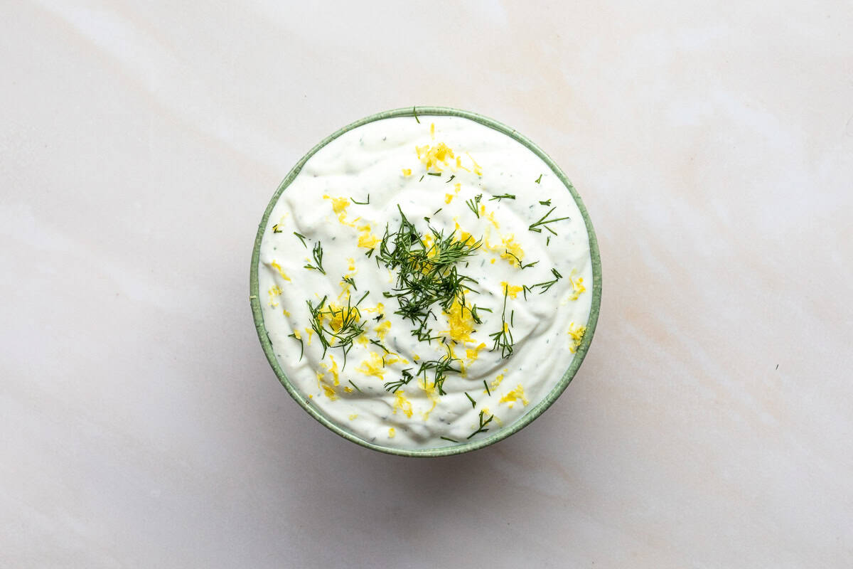 A bowl of creamy whipped ricotta with goat cheese dip garnished with chopped dill and grated lemon zest, placed on a light-colored surface.