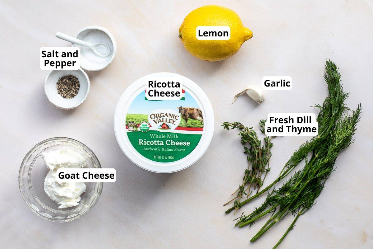 A spread of ingredients for a whipped ricotta recipe: salt and pepper, lemon, ricotta cheese, goat cheese, garlic, fresh dill, and thyme, all labeled on a light surface.