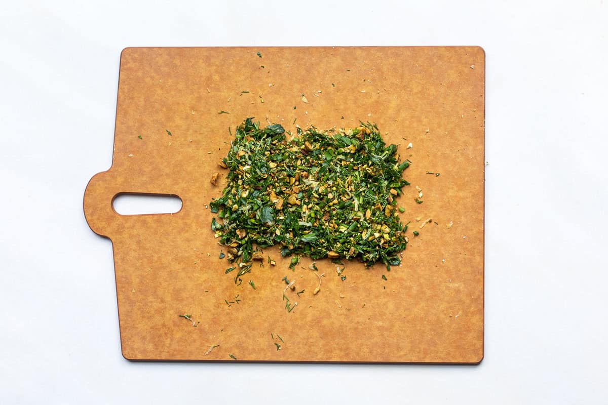 Chopped fresh dill, parsley, chives, pistachios and lemon zest on a cutting board.