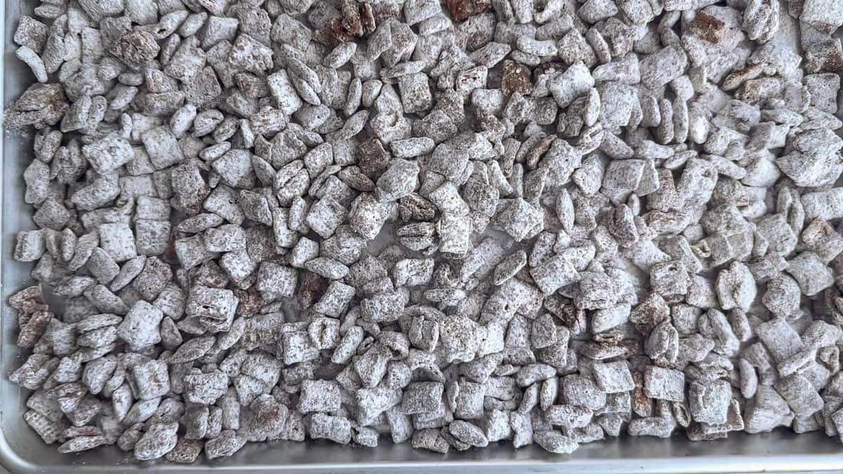 A baking tray filled with Chex cereal pieces coated in powdered sugar, commonly known as puppy chow or muddy buddies.