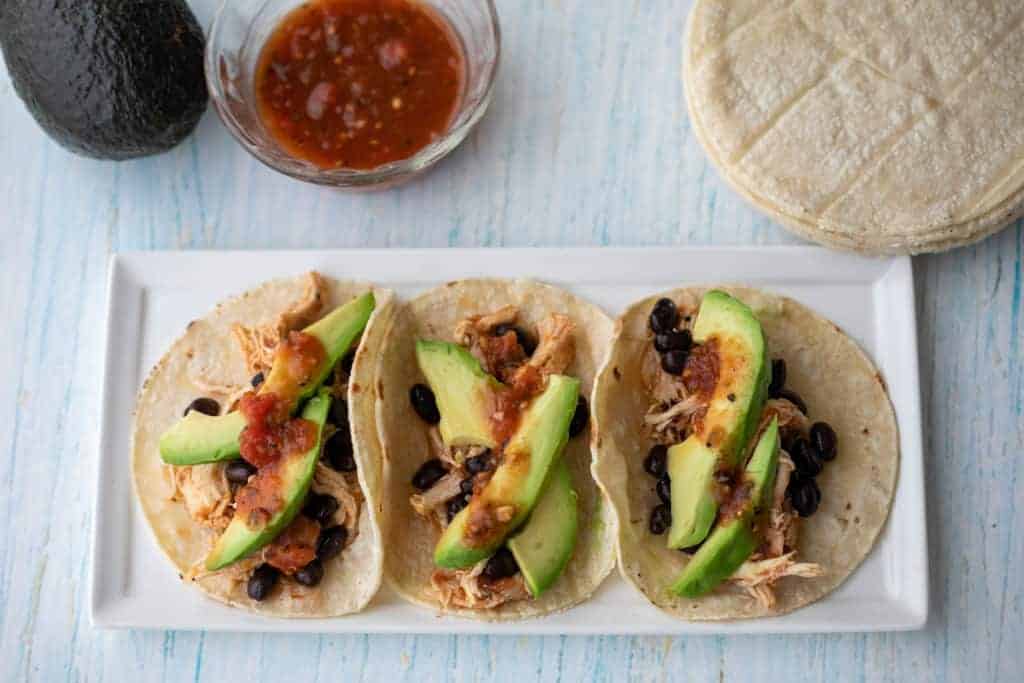 Three tacos filled with shredded chicken.