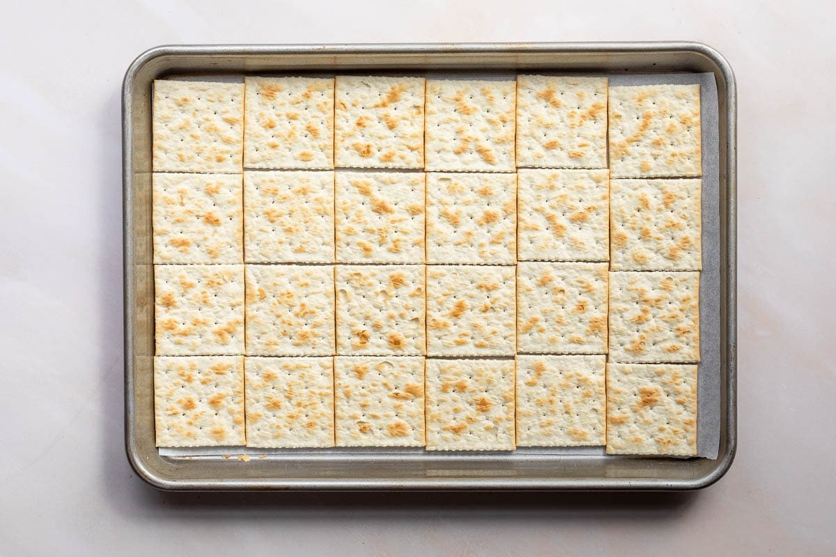 A baking sheet with 24 square saltine crackers arranged in a grid pattern.