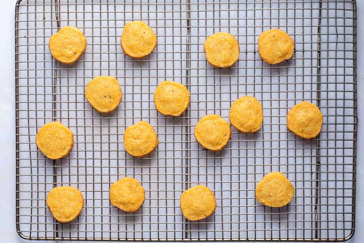 Fourteen cheese sables are evenly spaced on a metal cooling rack over a white background.