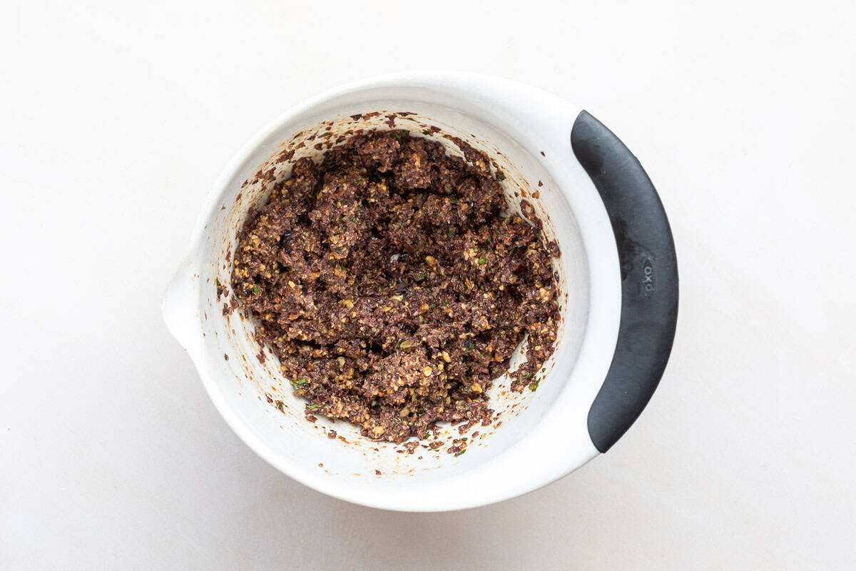 Olive tapenade mixed with toasted walnut pieces in a medium bowl.