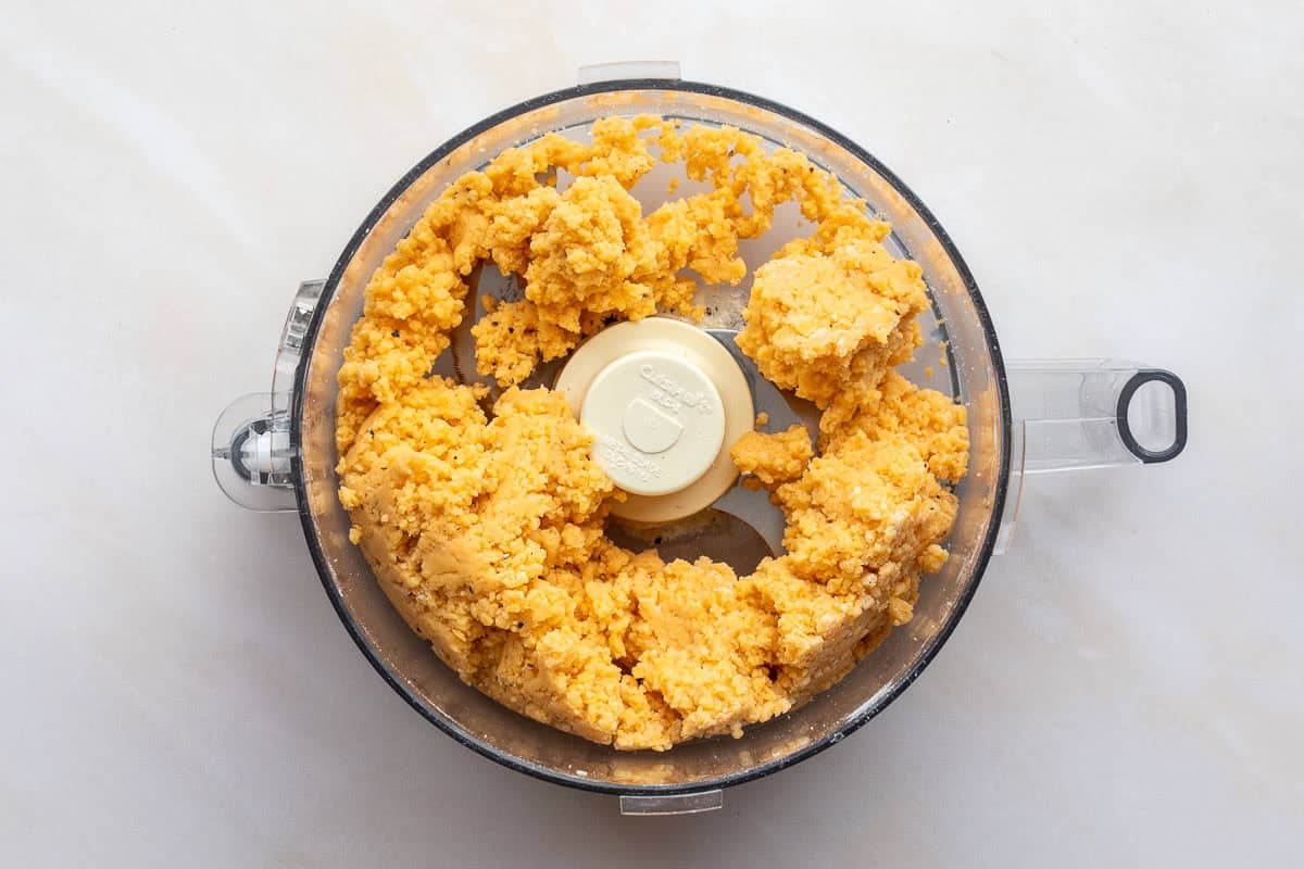 A food processor containing a cheese sable dough sits on a light-colored surface.