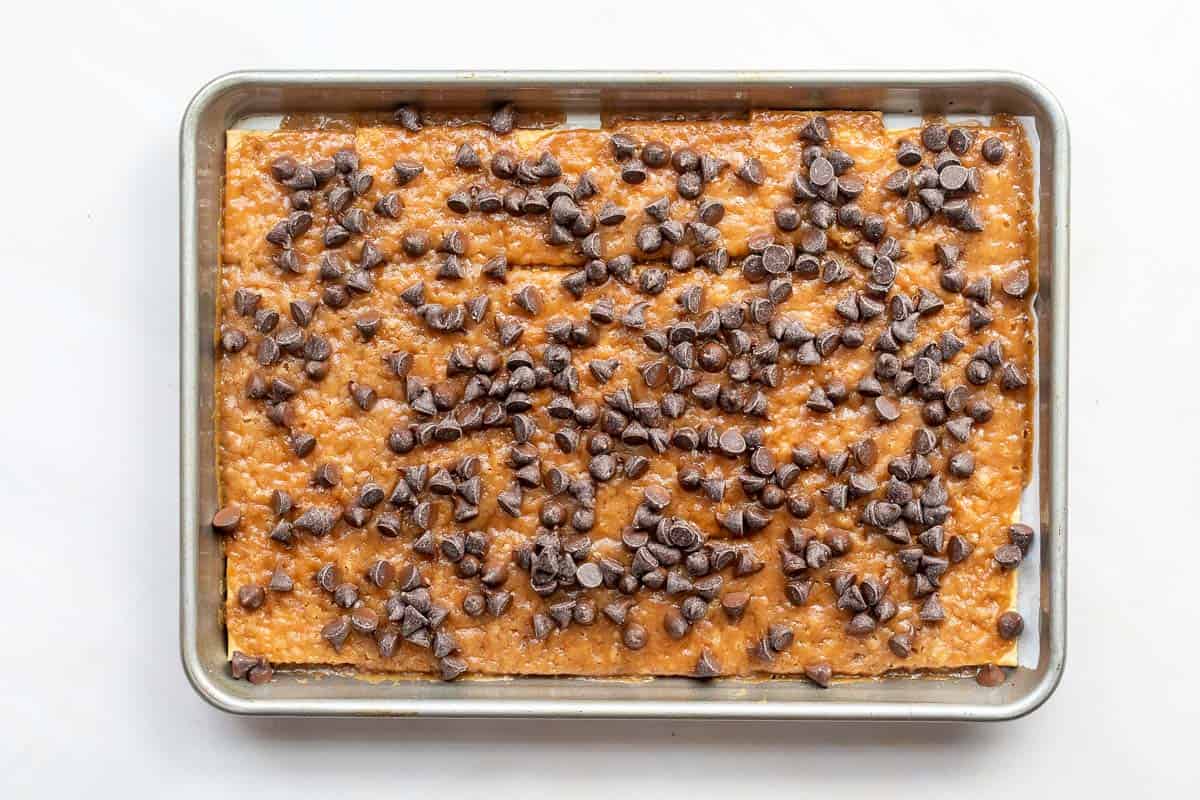 Toffee covered saltine crackers on baking sheet with chocolate chips on top.