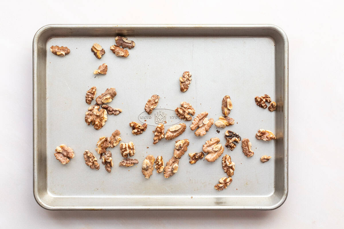 A metal baking sheet with scattered toasted walnut halves and pieces on a light background.