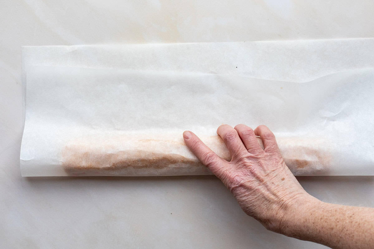 Hand wrapping log of cheese sable dough with parchment paper.