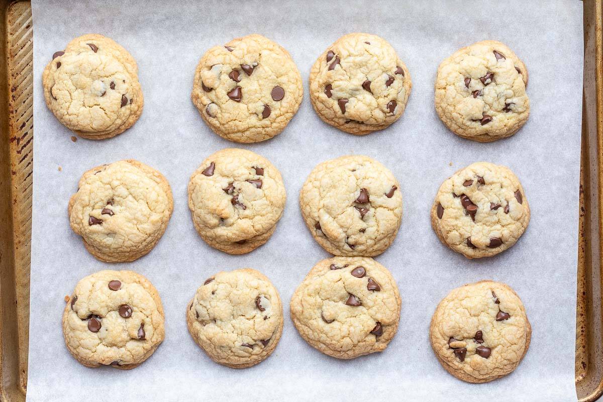 Twelve brown butter chocolate chip cookies are arranged in rows on a baking sheet lined with parchment paper.
