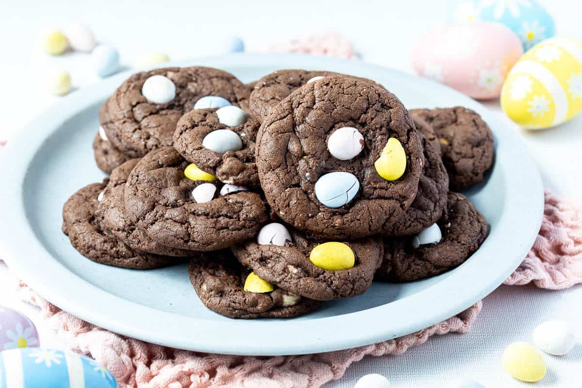 A plate of chocolate Cadbury mini egg cookies, surrounded by decorative Easter eggs.