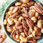 A bowl filled with assorted honey roasted nuts, including pecans, cashews, and almonds, seasoned with herbs.