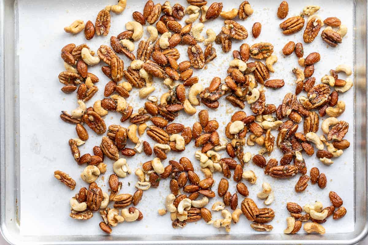 A baking sheet with a mix of roasted almonds, cashews, and pecans tossed in honey and sprinkled with sugar and salt spread out evenly.