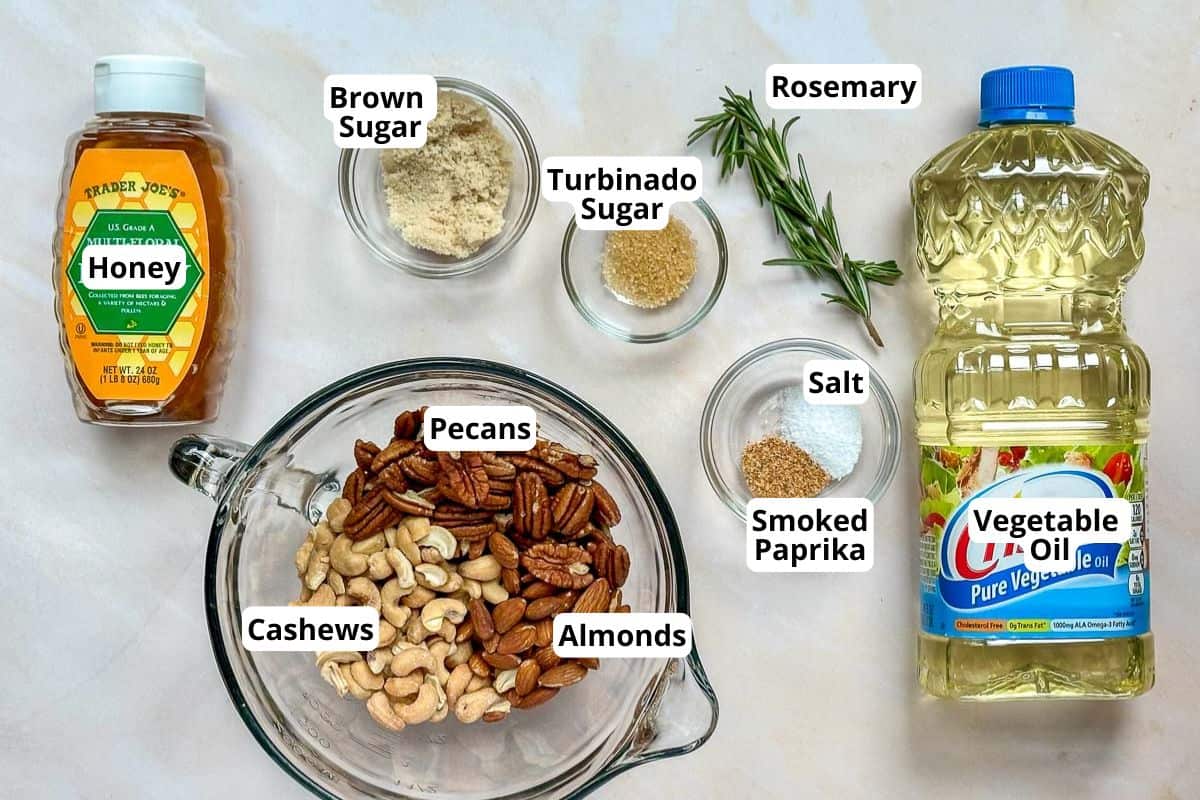 Assorted nuts, honey, brown sugar, turbinado sugar, vegetable oil, rosemary, salt, and smoked paprika arranged on a countertop.