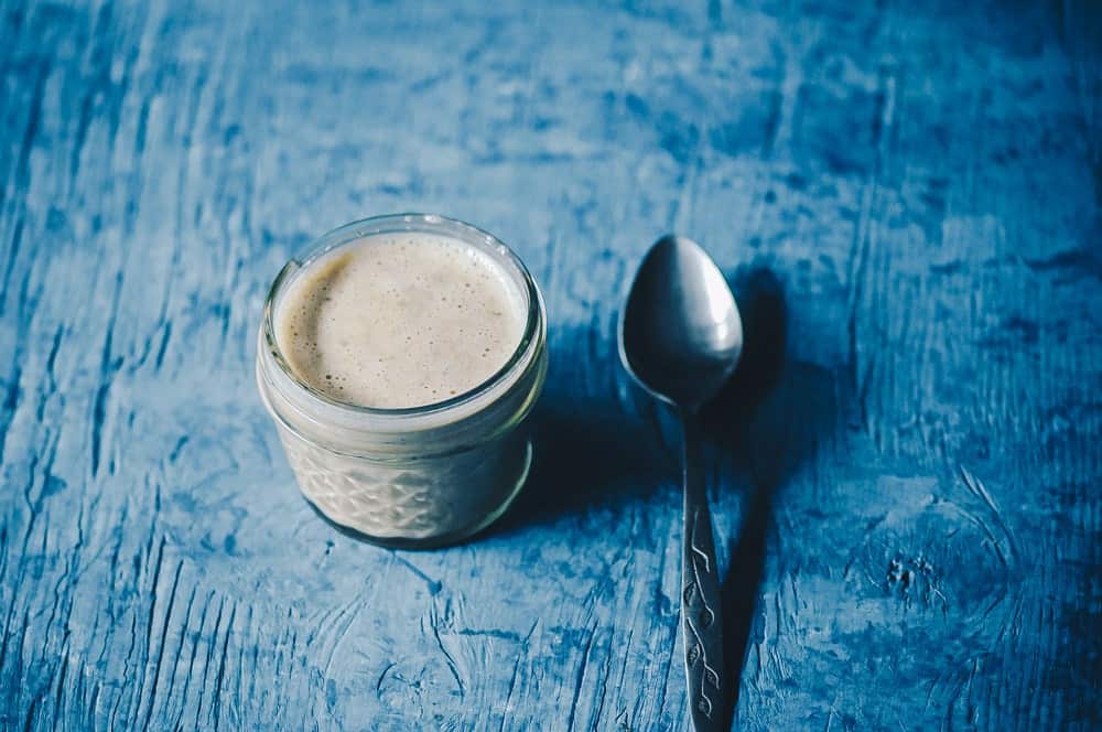 small jar of vegan pumpkin seed ranch dressing on blue wood background with spoon.