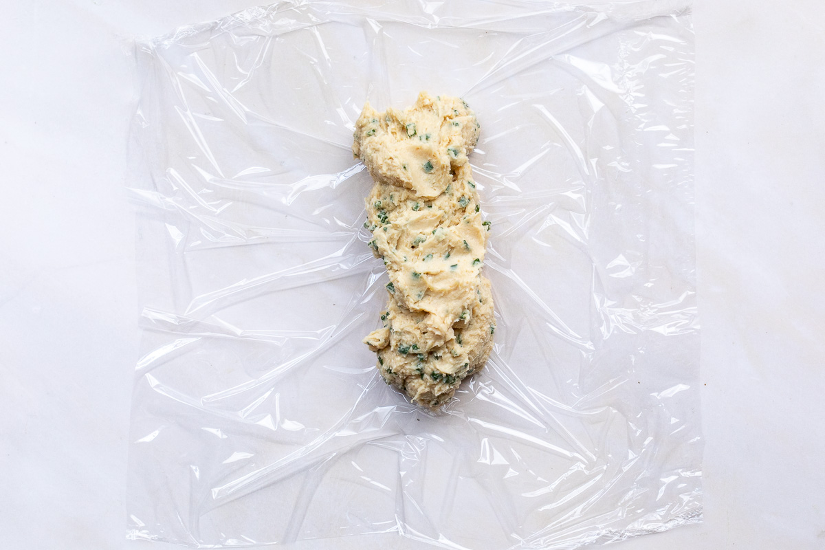 A log of miso butter with chives on a sheet of plastic wrap.