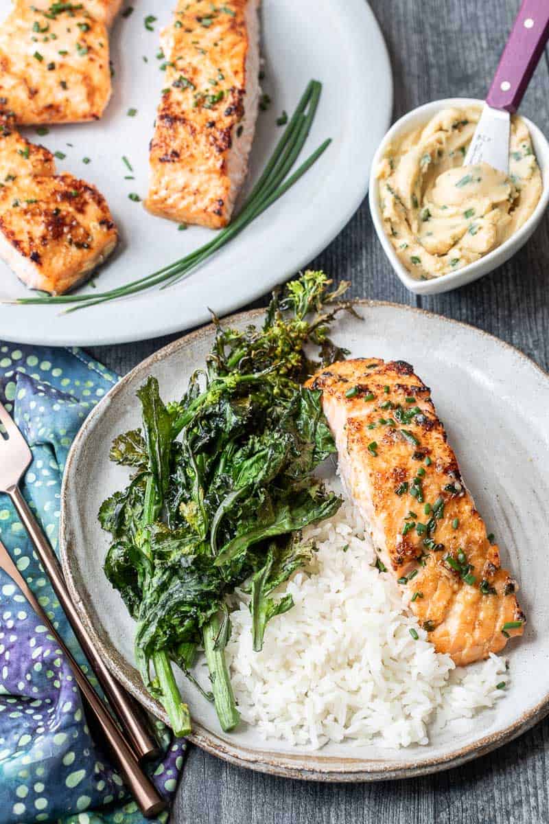Miso salmon fillet served with steamed white rice, crispy greens, and a bowl of miso butter; additional salmon pieces on a separate plate.