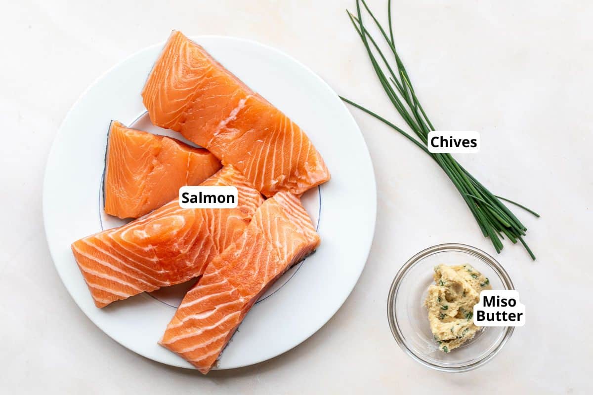 Four raw salmon fillets on a plate, fresh chives, and a small bowl of miso butter on a light surface. Each ingredient is labeled.