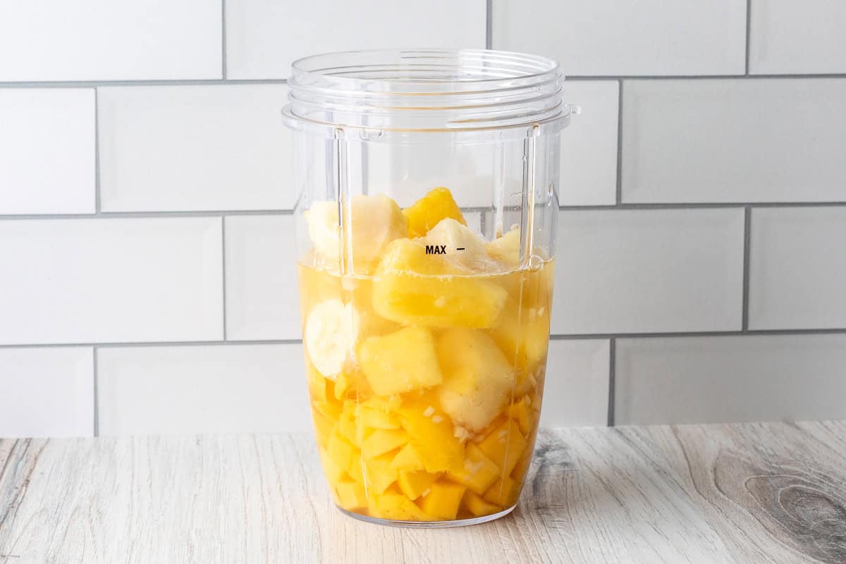 Ingredients for mango pineapple smoothie in blender cup.