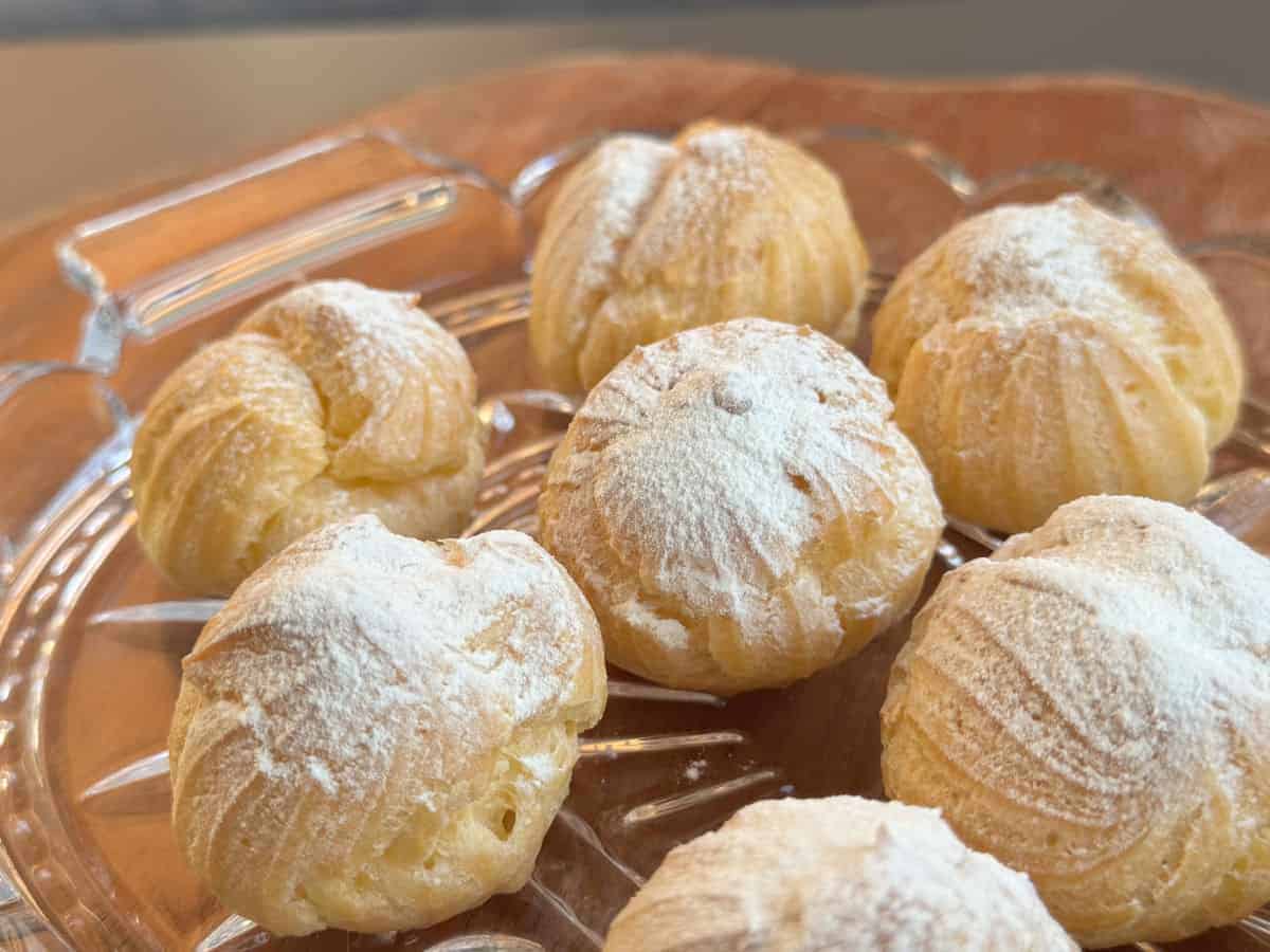 A glass plate holds several cream puffs dusted with powdered sugar.